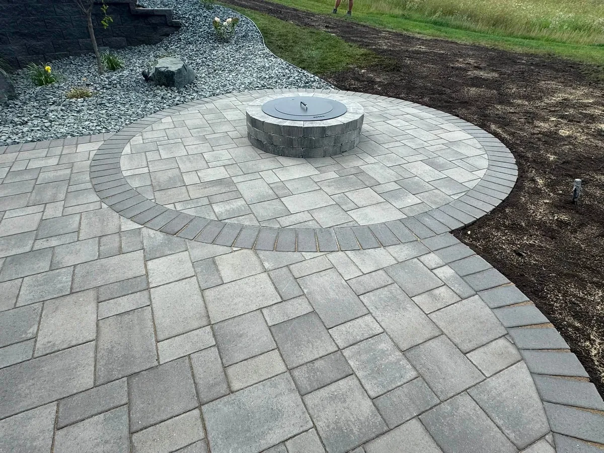 Round fire pit centered in a paver patio beside a rock garden in Southern Minnesota